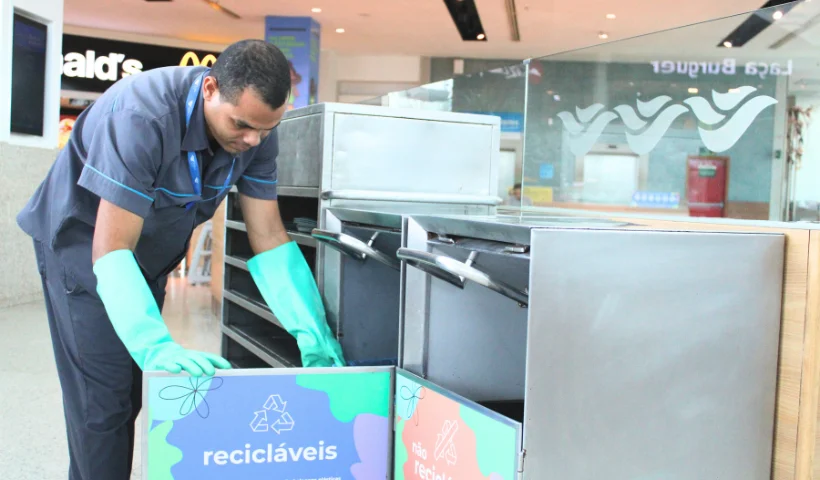 A imagem mostra um trabalhador separando o lixo de uma lata com uma arte escrito "Recicl&aacute;veis"