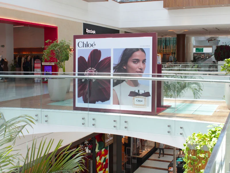 Painel gigante da campanha Chloé "The New Parfum" posicionado no corredor do shopping, visível de vários andares, com a modelo e o frasco icônico.
