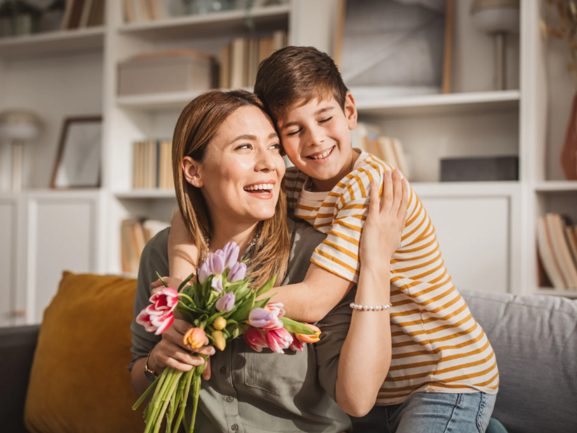 M&atilde;e e filho abra&ccedil;ados e sorridentes enquanto ela segura um buqu&ecirc; de flores