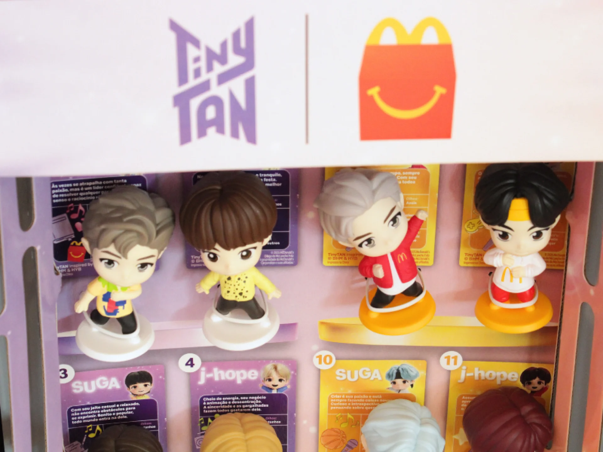 Dois bonecos de plástico, um com cabelo cinza e camisa amarela, o outro com cabelo castanho-escuro e camisa amarela. Eles estão em bases brancas. Dois bonecos de plástico, um com cabelo castanho claro e jaqueta amarela, e o outro com cabelo cinza claro. Eles estão em bases amarelas.