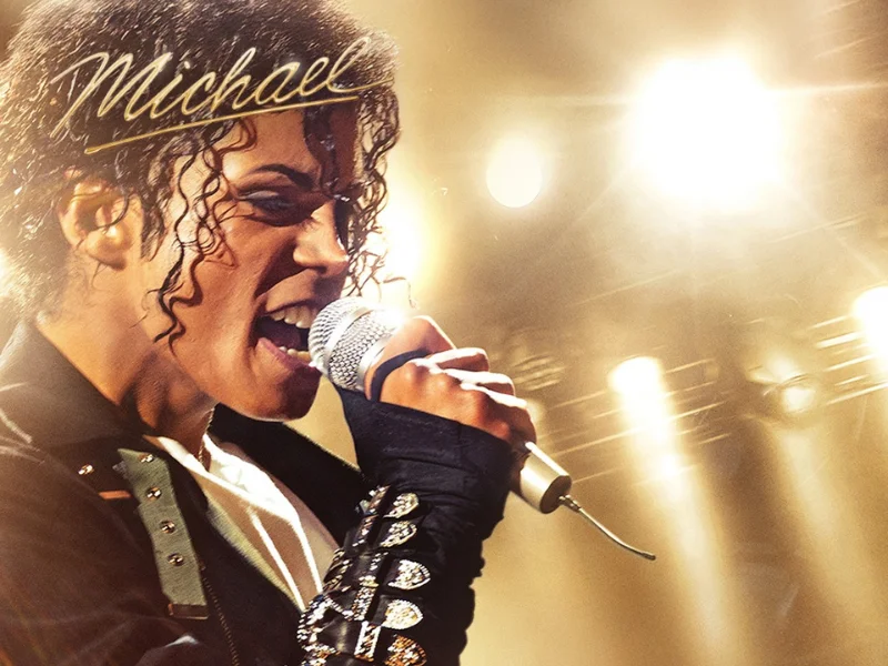 Pôster do filme "Michael" mostra o ator Jaafar Jackson caracterizado como Michael Jackson, cantando intensamente ao microfone sob luzes douradas de palco.