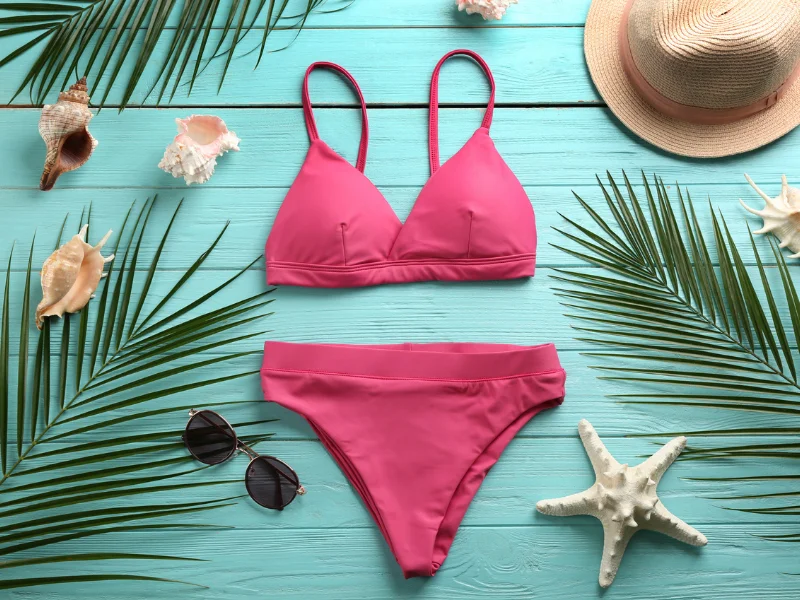 Conjunto de biquíni rosa vibrante sobre madeira azul-clara, decorado com conchas, óculos de sol, chapéu de palha e uma estrela-do-mar.