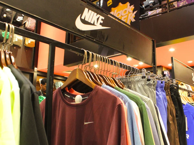 Um display de roupas da Nike em uma loja, com a arara sob um grande letreiro preto com o logo e nome da marca.
