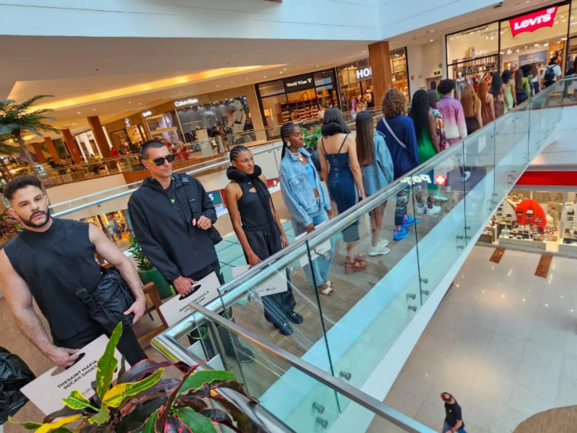 Modelos em fila em uma escada rolante de vidro. Eles exibem roupas casuais e urbanas. Modelos em fila em uma escada rolante de vidro. Eles exibem roupas casuais e urbanas.