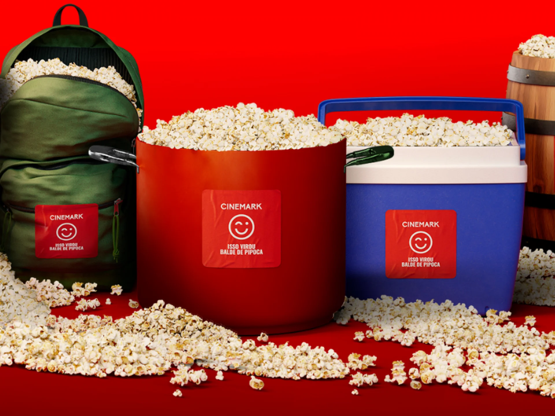 Uma mochila verde, uma panela vermelha e um cooler azul, todos transbordando pipoca sobre um fundo vermelho. Cada item possui um adesivo da Cinemark com o texto "Isso virou balde de pipoca".