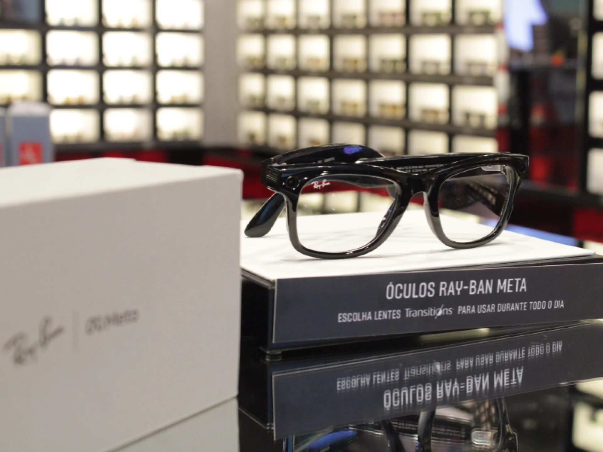 Óculos Ray-Ban de armação preta com lentes transparentes, repousando sobre sua caixa e uma folha explicativa com texto.