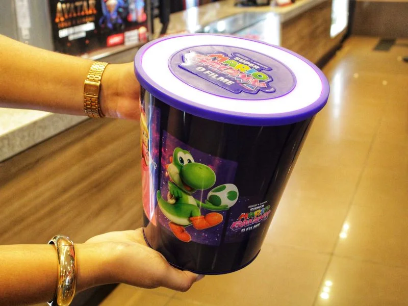A foto mostra um balde de pipoca tem&aacute;tico do filme "Super Mario Galaxy: O Filme" (t&iacute;tulo em portugu&ecirc;s no balde), segurado por uma pessoa no sagu&atilde;o do Cinemark.